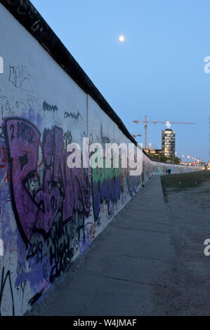 BERLIN - 18 APRIL 2019: Symbols of Germany:preserved section of Berlin Wall at the East Side Gallery with a giant crane and a Mercedes Benz building Stock Photo
