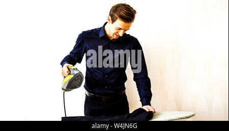 Young man ironing clothes on ironing board in home. Housework concept. Stock Photo