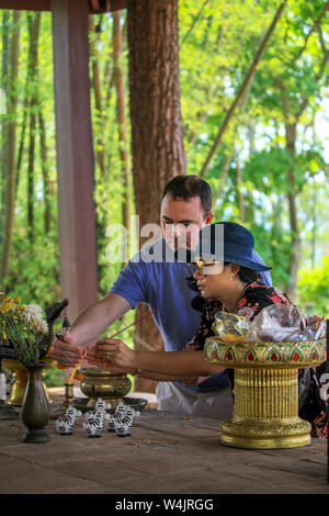 An American Thai husband and wife light votive candles at the 800-year old ancient Buddhist temple of Wat Ku Din Khao in the Chiang Mai Zoo, Thailand. Stock Photo