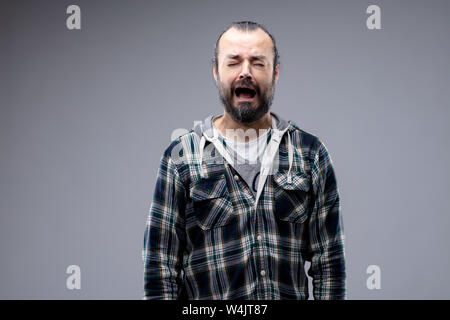 Miserable tearful man wailing and crying with a woeful expression and closed eyes isolated on grey with copy space Stock Photo