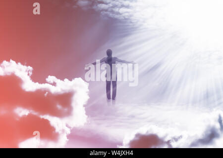 Silhouette of a man flying up in the sky in the bright rays of the sun with arms spread apart. Stock Photo