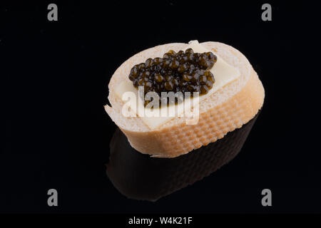 Black caviar on fresh baguette with butter, black mirror background. close-up. Stock Photo