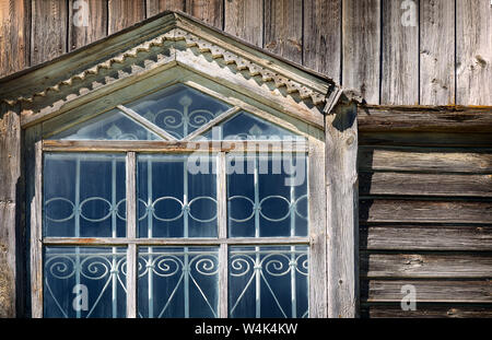A fragment of the window of the ancient Orthodox wooden Church with wrought iron bars and carved wooden platbands Stock Photo