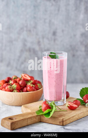 Strawberry smoothie in glass jar and fresh strawberries in wooden bowl on cutting board