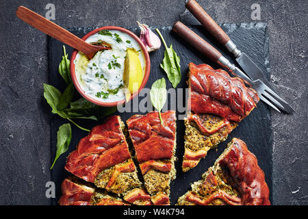 close-up of sliced Spinach Ricotta Pie on a black slate tray with tzatziki sauce in a bowl on a concrete table, view from above, flat lay, macro Stock Photo