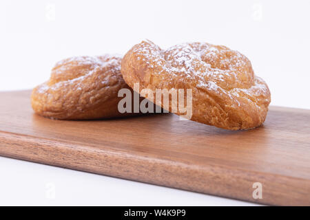 Side view of two delicious puff pastries with powdered sugar on top of a cutting board on a white background. Stock Photo