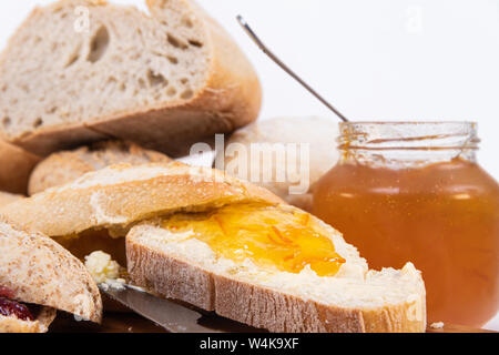 a jar of jam, freshly baked piece of multigrain bread with sunflower seeds and more breads in the background Stock Photo