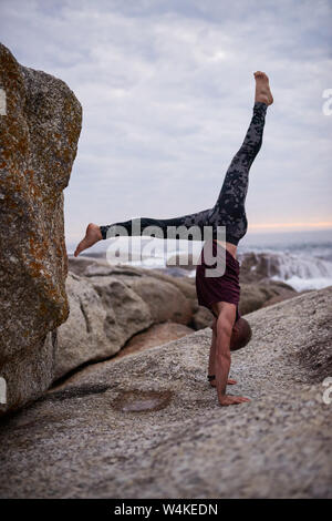 Man doing a hand stand by rocks while practicing yoga Stock Photo