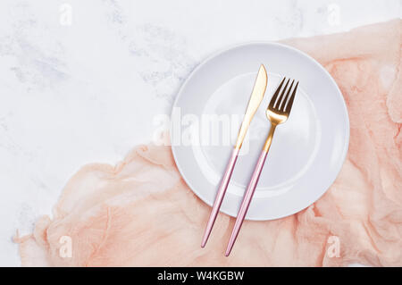 Empty white plate and modern design cutlery on the white marble table, top view Stock Photo