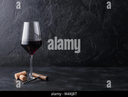 Elegant glass of red wine with corks and corkscrew on black stone background. Stock Photo