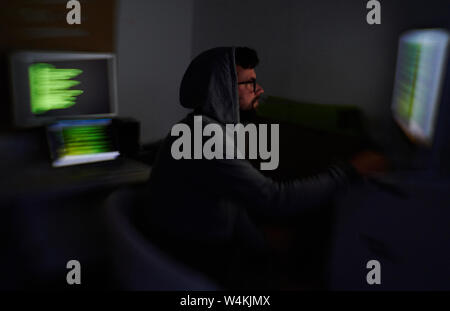 Berlin, Germany. 16th July, 2019. A man in a hooded sweater looks into a screen. Behind him are further screens with green luminous writing. Credit: Annette Riedl/dpa-Zentralbild/dpa/Alamy Live News Stock Photo