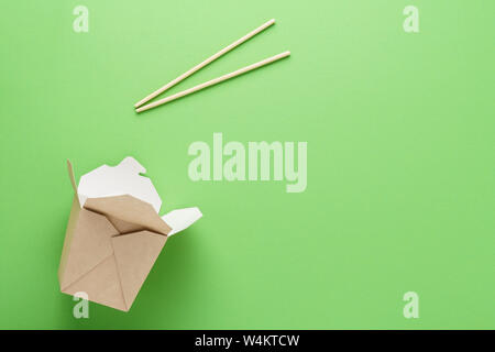 Open empty kraft paper box and chopsticks on green background. Food delivery concept. Copy space. Stock Photo