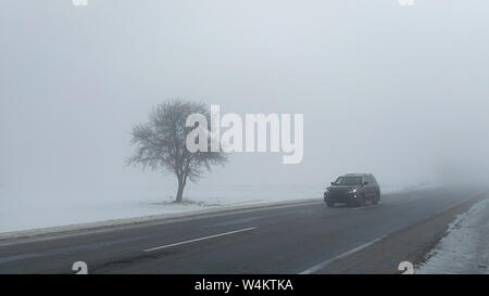 Cars in the fog. Bad winter weather and dangerous automobile traffic on the road. Light vehicles in foggy day. Stock Photo
