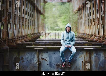 Lonely man looking at smartphone on abandoned rusty bridge. Stock Photo