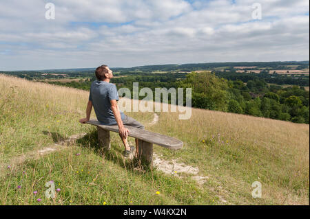 Old gnarled bleached wooden seat park bench, on hill in chalk grassland facing south towards Northdowns enjoying the view and sunshine Stock Photo