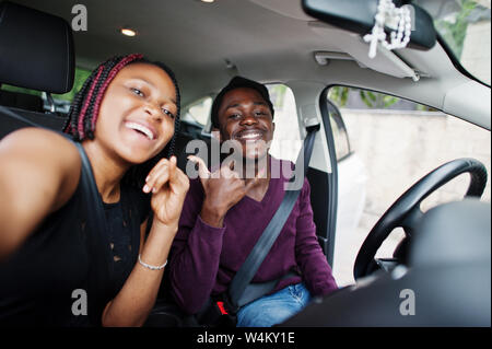 Beautiful young african american couple sitting on the front passenger seats while handsome man driving a car. Making selfie together. Stock Photo
