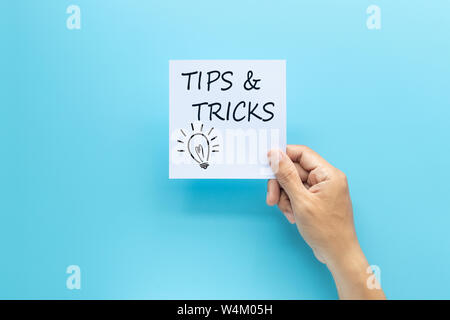 text tips and tricks on white paper in hand isolated on blue background Stock Photo