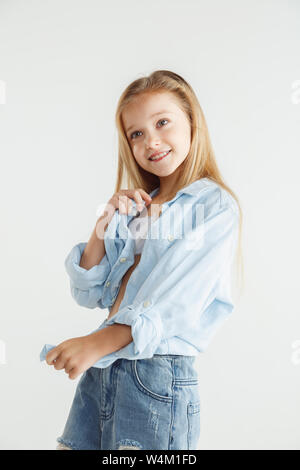 Stylish little smiling girl posing in casual clothes isolated on white studio background. Caucasian blonde female model in shirt and jeanse. Human emotions, facial expression, childhood, fashion. Stock Photo