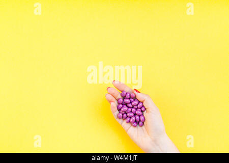 Woman hand holding purple pills handful isolated on bold yellow background with copy space. Template for feminine beauty blog social media. Female hea Stock Photo