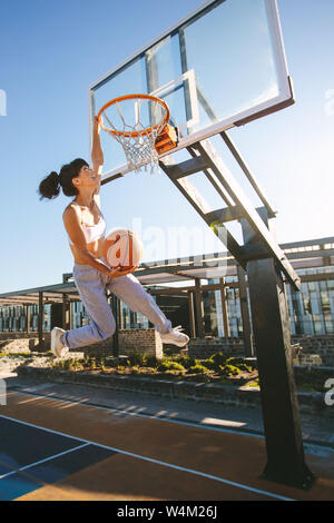 Female playing basketball outdoors on summer day. Woman basketball player making slam dunk. Stock Photo