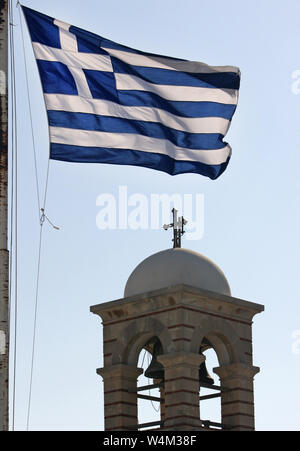 Greek flag waving in the wind with a church  tower in the background Stock Photo