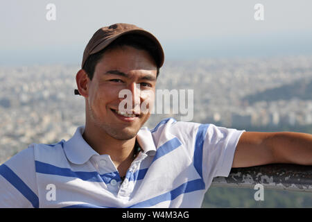 Handsome and smiling young man wearing a baseball cap sitting in the sun Stock Photo