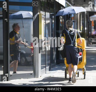 24 July 2019, Hessen, Frankfurt/Main: Under an umbrella mounted on his delivery van, mail carrier Erwin Desch protects himself from the hot Somme while delivering mail in summer clothes in the Bornheim district. Germany is facing a heat wave - and already on Wednesday this will be clearly noticeable in many areas. Photo: Arne Dedert/dpa Stock Photo