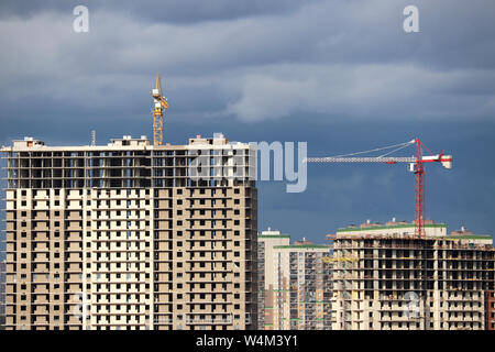 Construction cranes and high-rise residential building under construction on background of storm sky with clouds Stock Photo