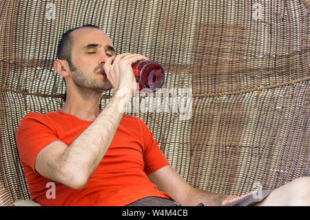 Man with orange t-shirt drinking alcohol straight from the bottle. Alcoholism concept. Stock Photo