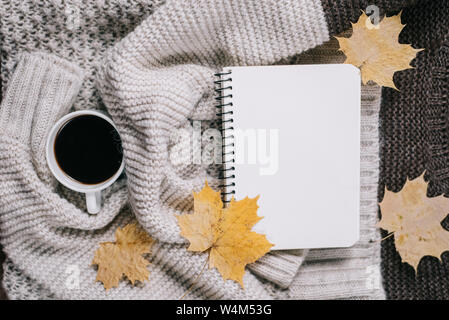 Knitted sweater, cup of coffee, notebook, autumn maple leaves on brown background. Flat lay, top view, copy space. Women clothing. Stock Photo