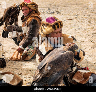 Altai eagle festival. Hunters are  sitting with their  Golden Eagles on the Hand. Close up. Main focus on  man which  is in the foreground Stock Photo