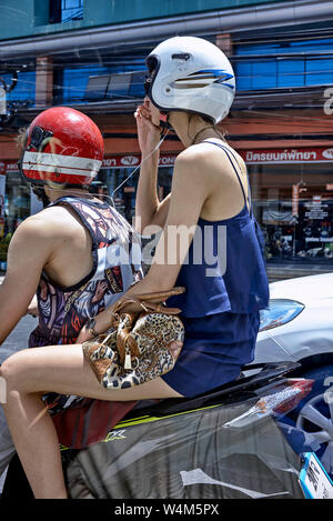 Woman motorcycle. Female riding pillion on a motorbike and sharing music from her smartphone, via headphones, with the male rider. Stock Photo
