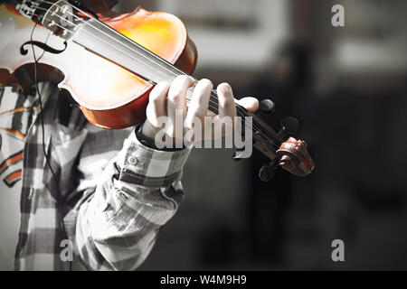A skilled violinist, dressed in a plaid shirt and a white t-shirt with an orange pattern, plays a melody on an old beautiful violin. Stock Photo