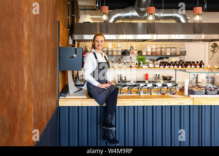 Happy successful small restaurant owner sitting on counter proud of her small business Stock Photo