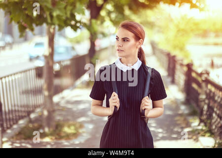 Student girl outdoors walking on sidewalk going to school – college woman with backpack and uniform smiling – education concept with trendy teenage fe Stock Photo