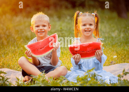 children on the lawn with slices of watermelon in their hands in the rays of sunset Stock Photo