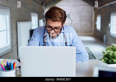Handsome hipster working on his laptop in modern, industrial office Stock Photo