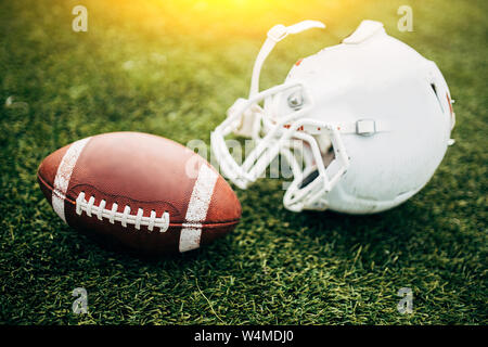 Image of white helmet of Amerinian football player and ball on green lawn Stock Photo