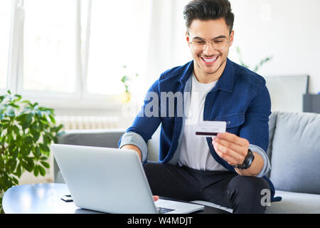 Cheerful young man using credit card and laptop to pay for shopping online Stock Photo