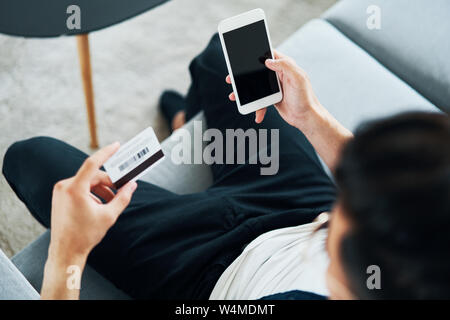 Overhead view of young man using smartphone and credit card to do shopping online Stock Photo