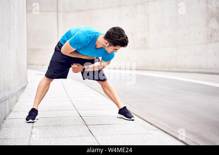 Athletic man bending forward doing exercises during urban workout session Stock Photo
