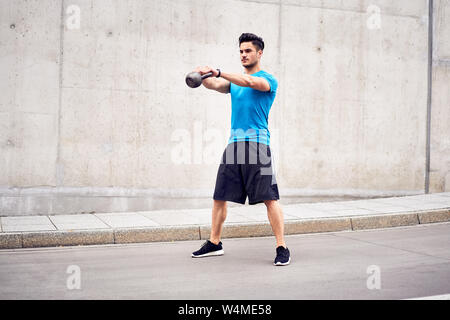 Health and fitness concept. Man doing kettlebell swing exercises during urban workout session Stock Photo
