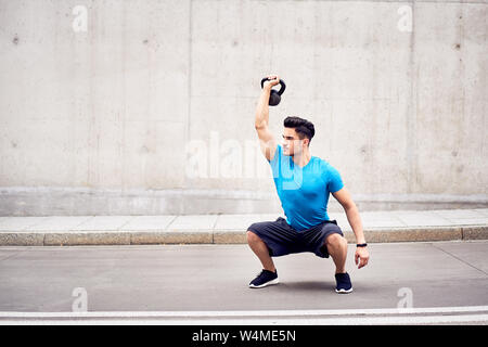 Athletic man doing kettlebell squatting exercises outdoors in the city Stock Photo