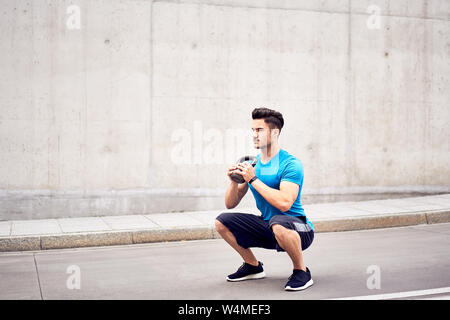 Muscular man doing squats with kettlebell in the city Stock Photo