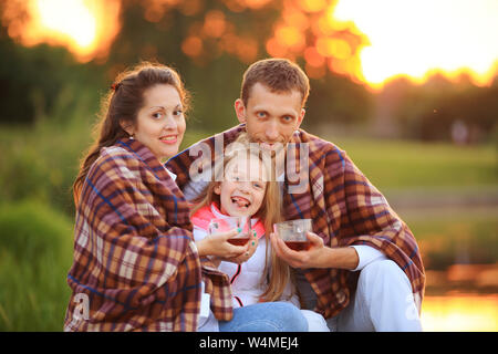 happy family wrapped in a blanket drinking hot tea sitting on a bench in the cool autumn day .the photo has a space for your text Stock Photo