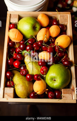 Photo from above of wooden box with cherries, apples, apricots, pear on table Stock Photo