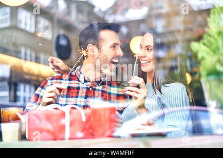 Couple playing with sparklers while sitting with present in cafe during Christmas time Stock Photo