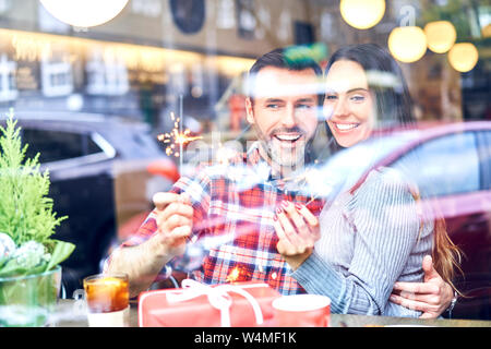 Couple sitting in cafe during Christmas and playing with sparklers Stock Photo