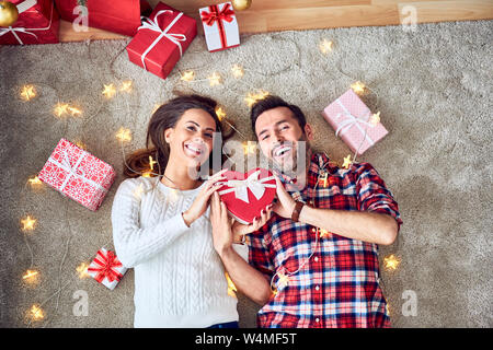 Cheerful couple having fun during christmas. Lying on floor decorated with lights and sharing presents Stock Photo