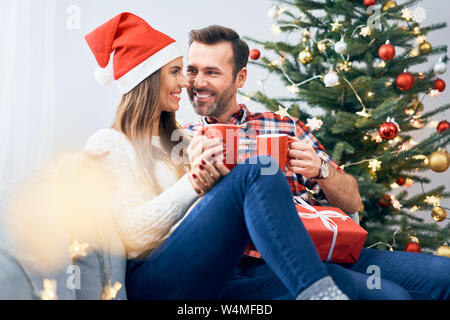 Cheerful couple relaxing together with mug of hot beverage during christmas celebration at home Stock Photo
